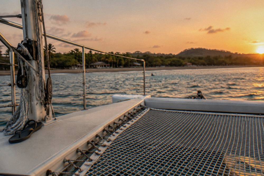 A wide catamaran deck with nets and railing under an open sky near golden hour