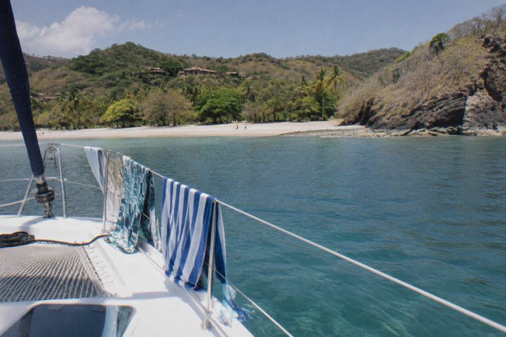 A catamaran at anchor in a calm bay with passengers' towels drying on the railing