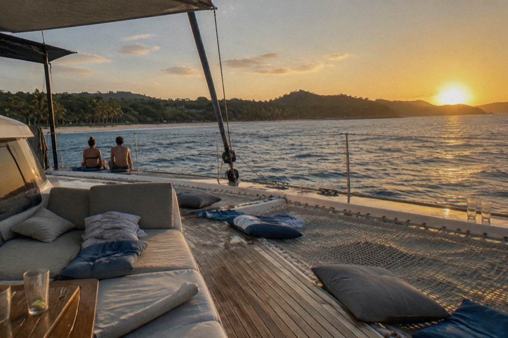 A wide catamaran deck with nets and seating in golden evening light on open water