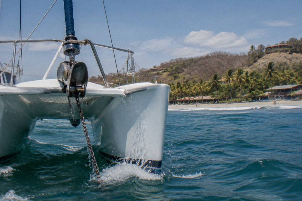 A catamaran bow cutting through small blue waves with spray along the hull