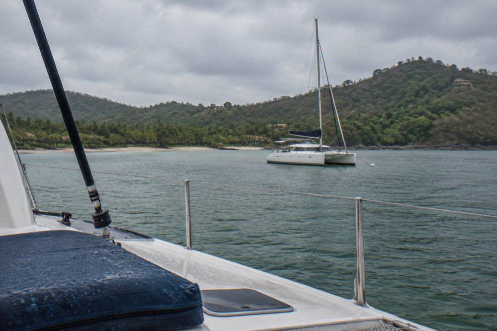 A moored catamaran in a calm protected bay with green forested hills behind it