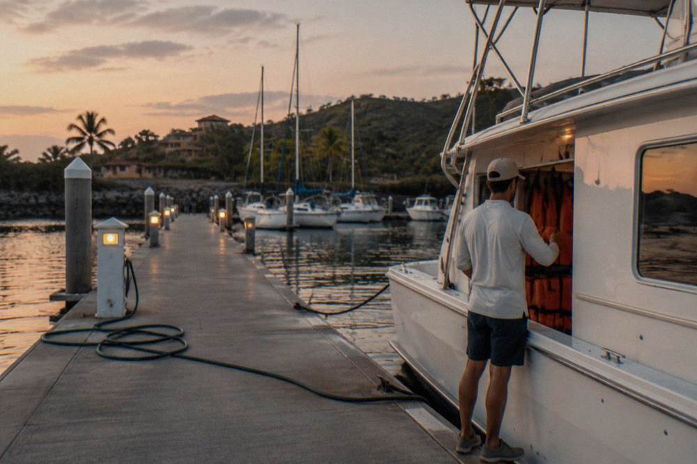 A crew member checking orange life jackets stowed along the side of a boat cabin