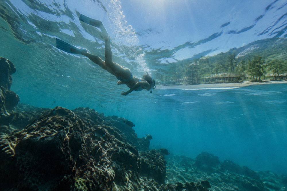 Snorkeler floating in clear turquoise water above a rocky reef