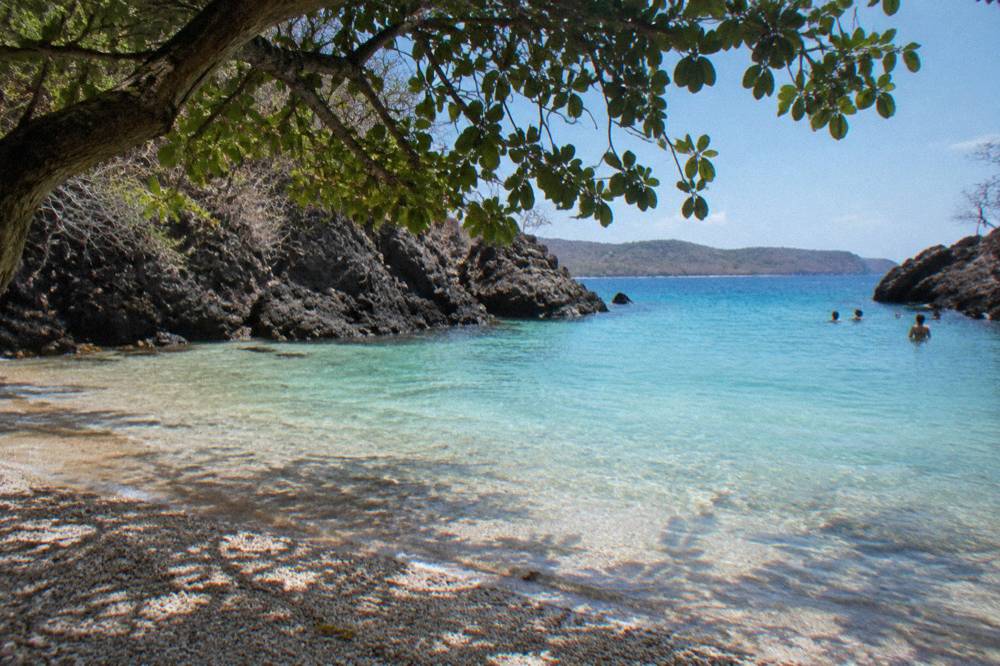 Small sandy cove with still turquoise water enclosed by dark rock headlands