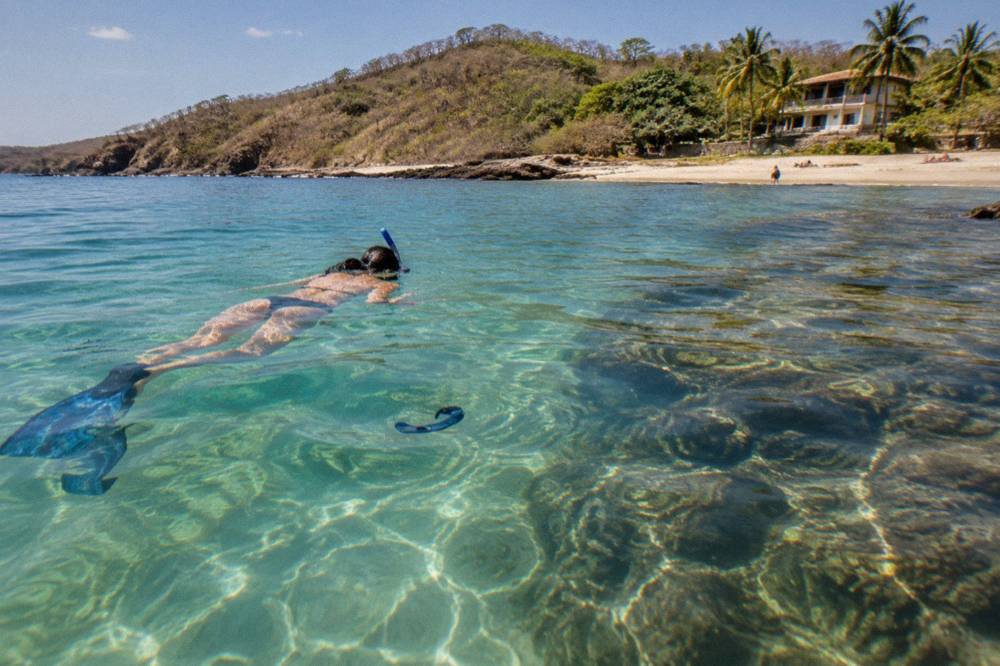 Snorkeler floating above clear shallow water over a rocky reef near Tamarindo
