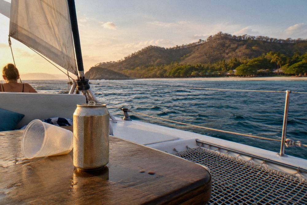Catamaran deck with passengers' drinks on a table and coastline in the background