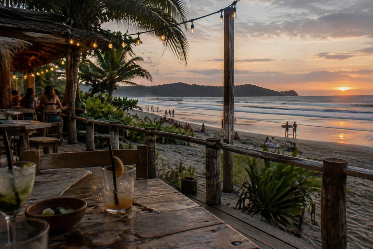 Beach bar deck with string lights above darkening sand as the sun sets over the Pacific
