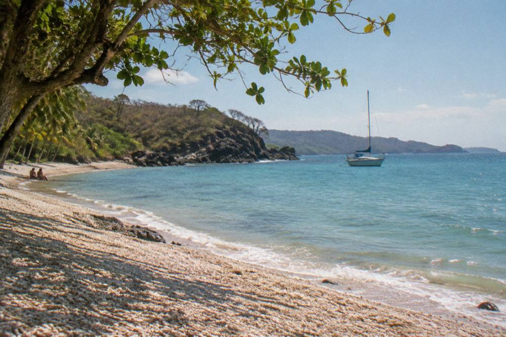 Anchored sailboat resting in clear turquoise water near a rocky point