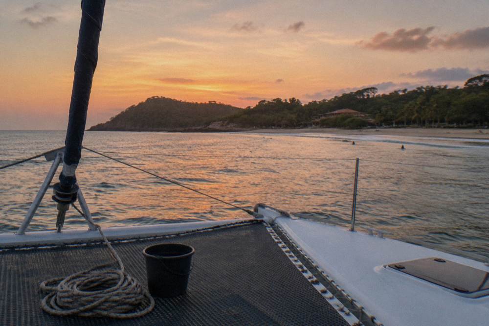 Catamaran with furled sails drifting on open water under a wide evening sky
