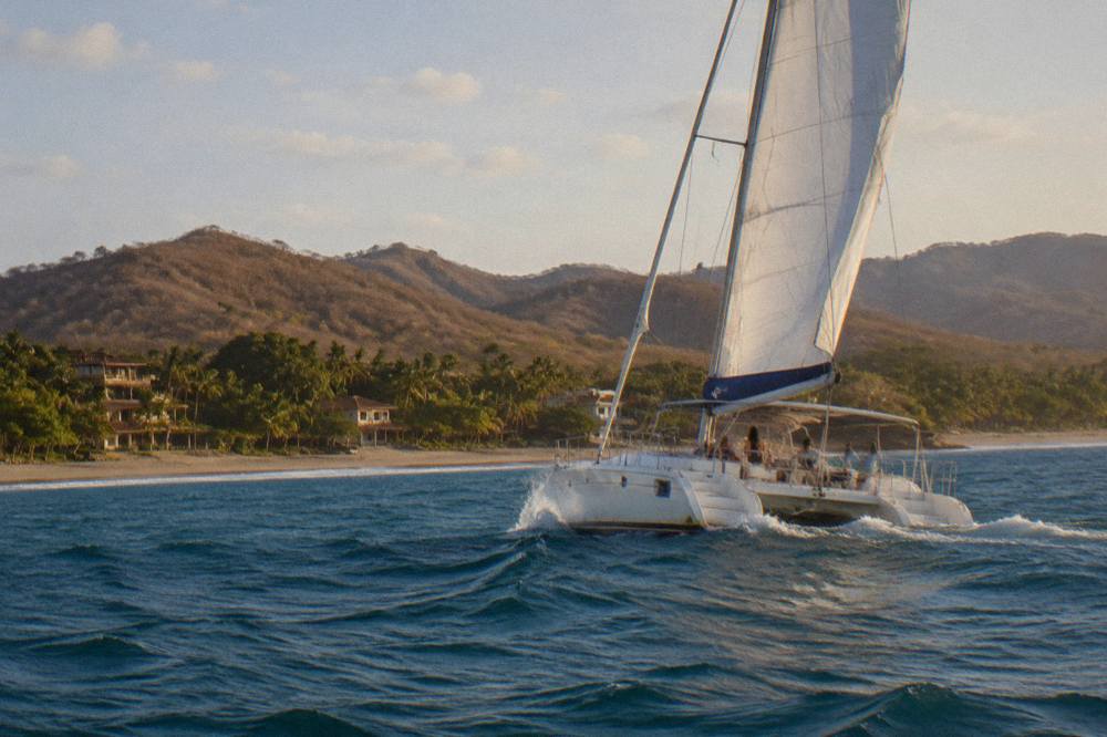 A cruising catamaran under sail on open Pacific water in late afternoon light