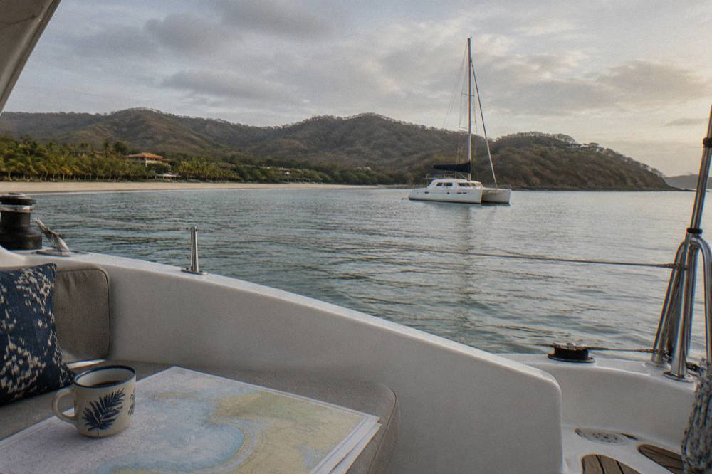 A catamaran at anchor in a quiet bay with forested hills behind it