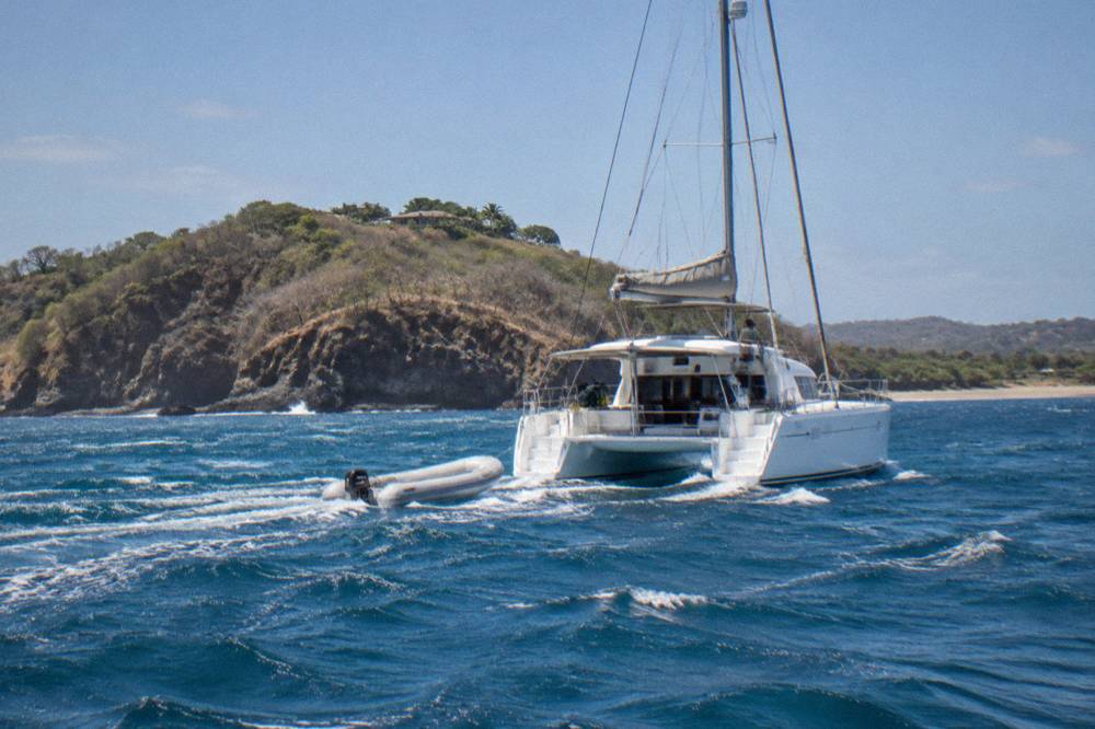 A catamaran deck with a dinghy alongside and open water beyond