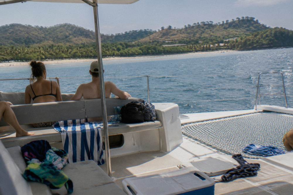 A shaded catamaran deck with bench seating and a view of open water