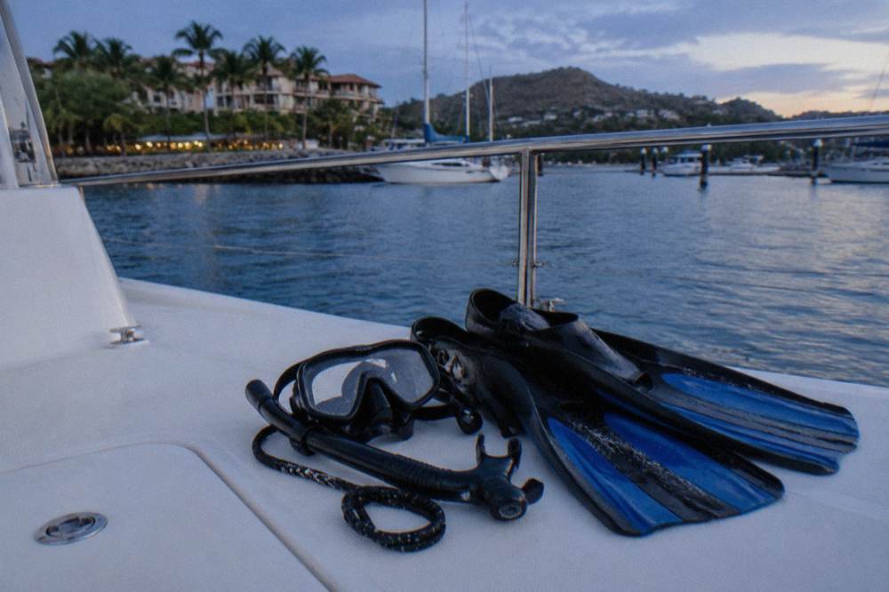 Snorkel mask and fins resting on a boat deck with blue ocean beyond the rail
