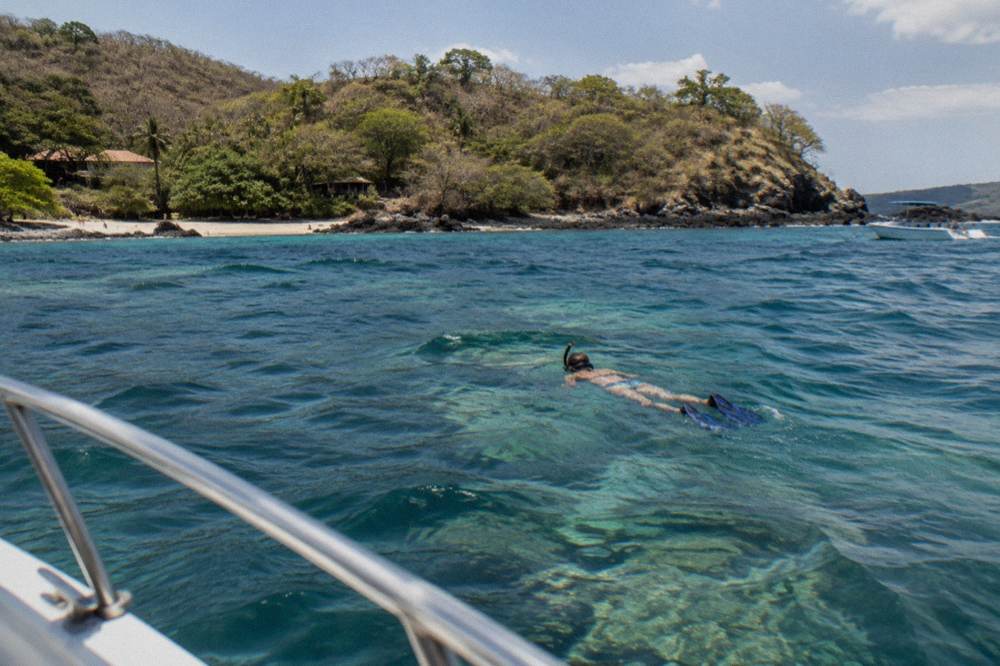 Snorkeler floating over clear shallow water above a rocky reef in late morning sun
