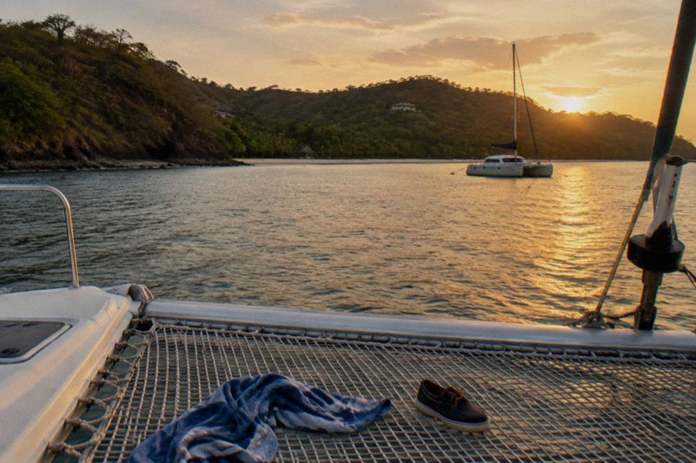 A wide catamaran deck at anchor in a calm bay with golden late afternoon light on the water