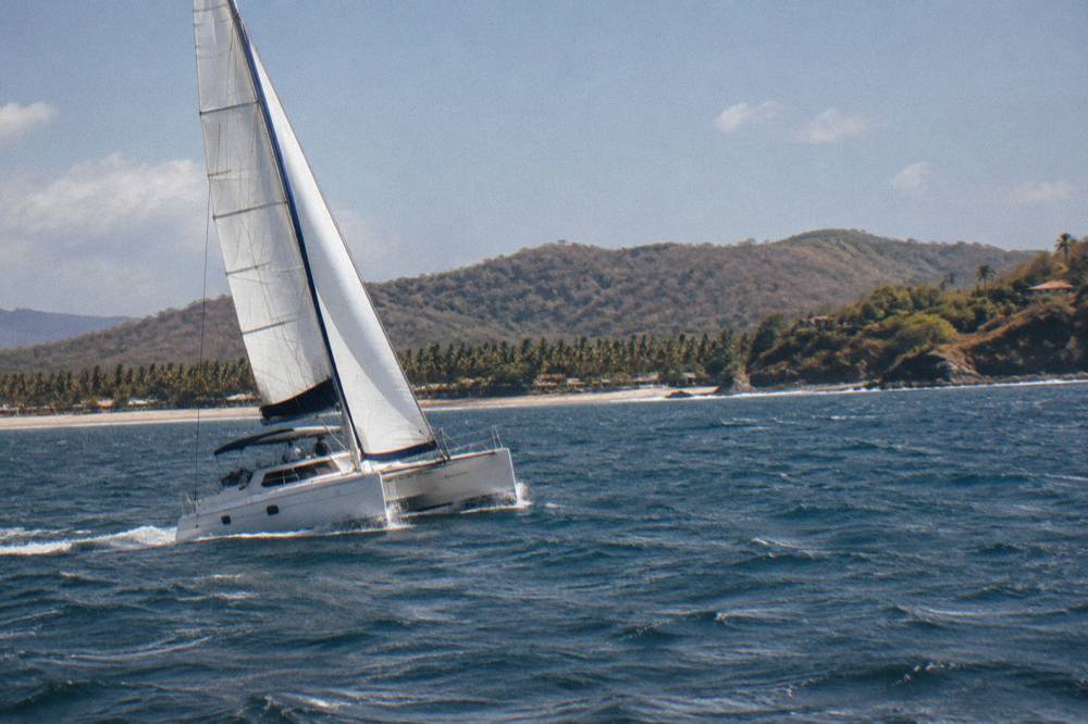White catamaran under sail on open Pacific water with small wind waves