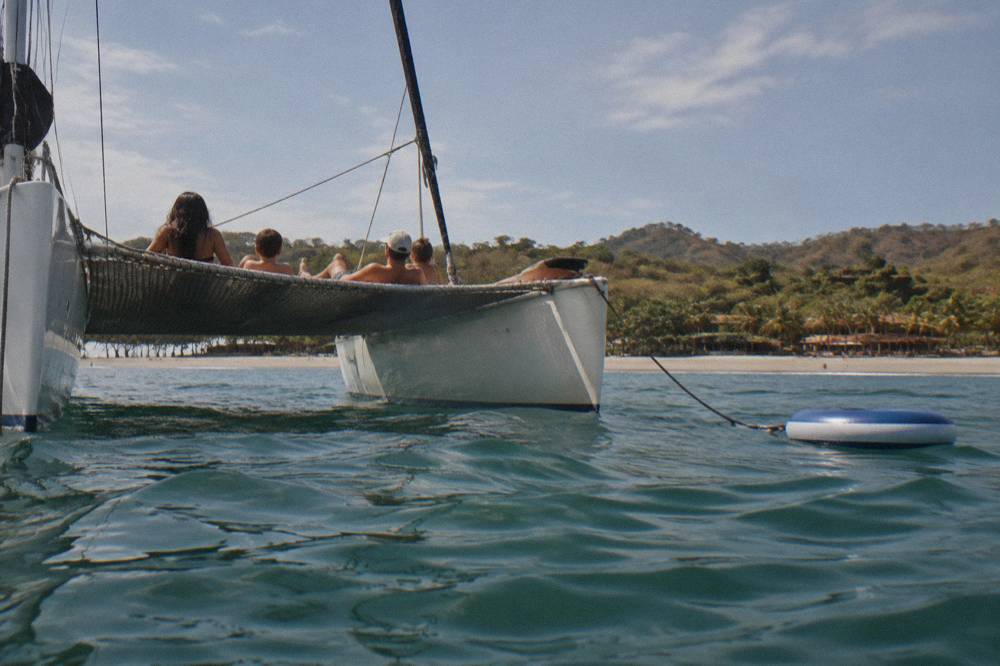Family relaxing on the trampoline net at the bow of a catamaran in calm water near Tamarindo