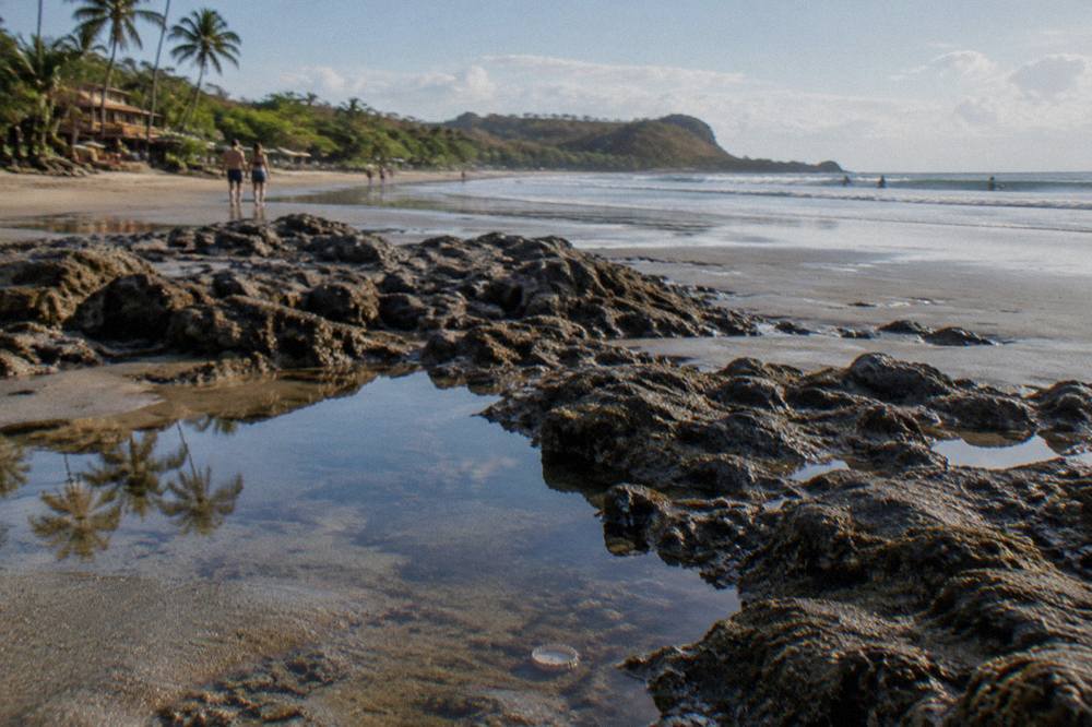Wide sandy beach at low tide with rocky outcrops and small tide pools reflecting the sky