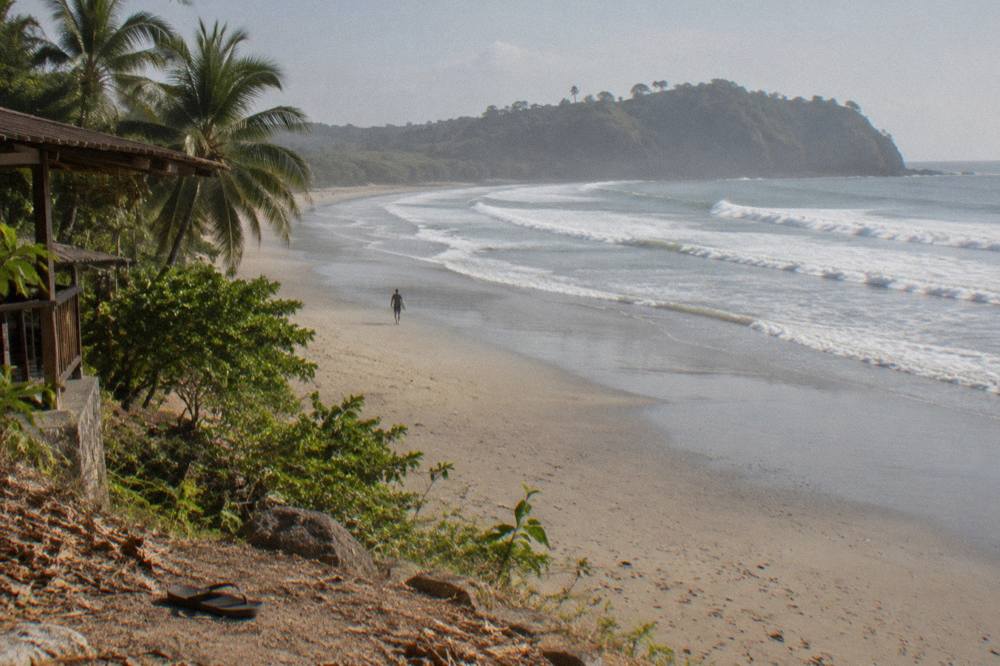 Wide empty beach with rolling surf and forested headland in the distance