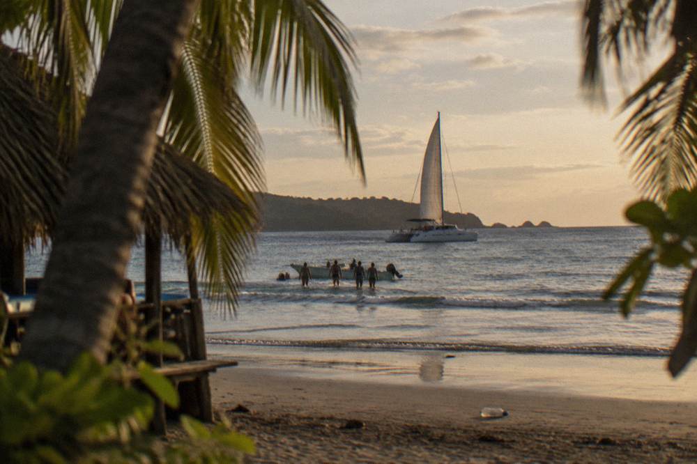 Catamaran under sail off a Pacific beach in late afternoon light