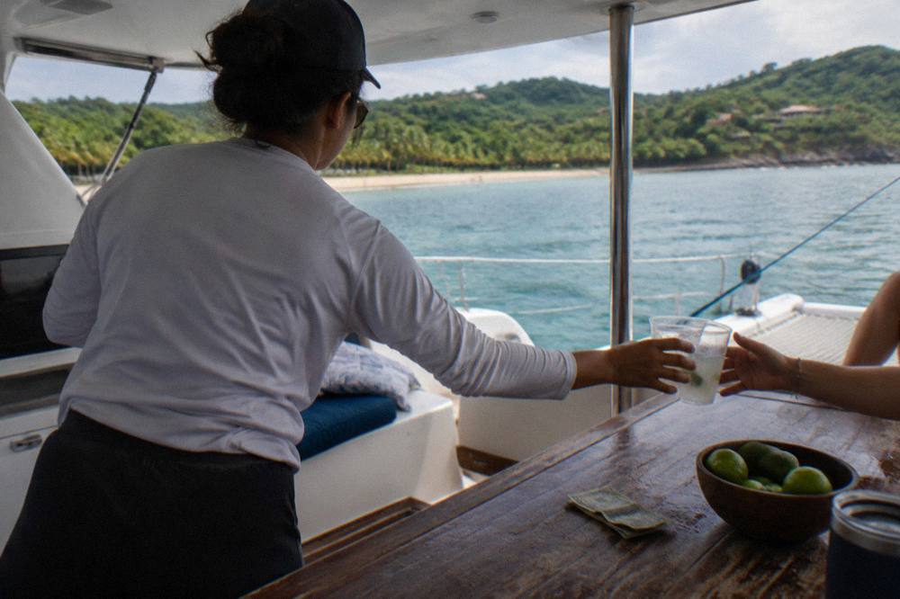 Crew member handing a drink across a catamaran deck table