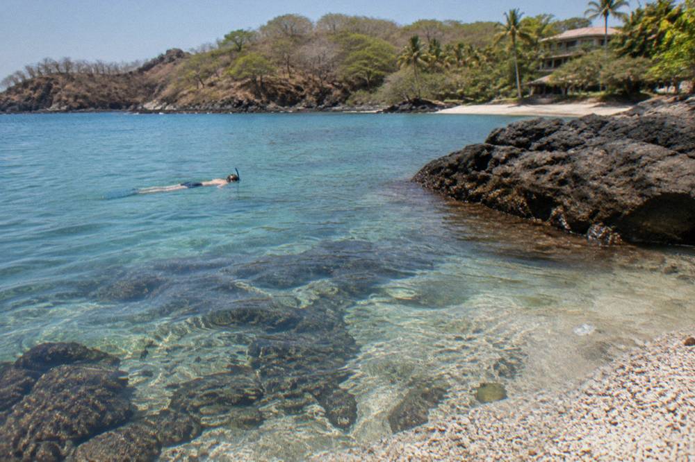 Snorkeler floating over clear shallow water above rocky reef