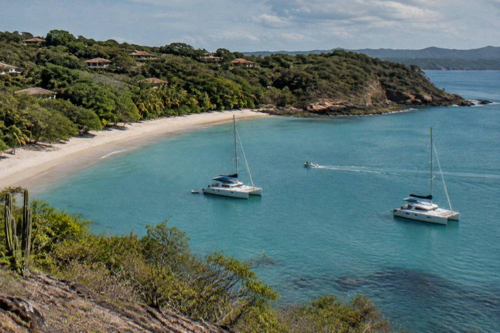 Two anchored catamarans in a calm bay with pale sand beach behind