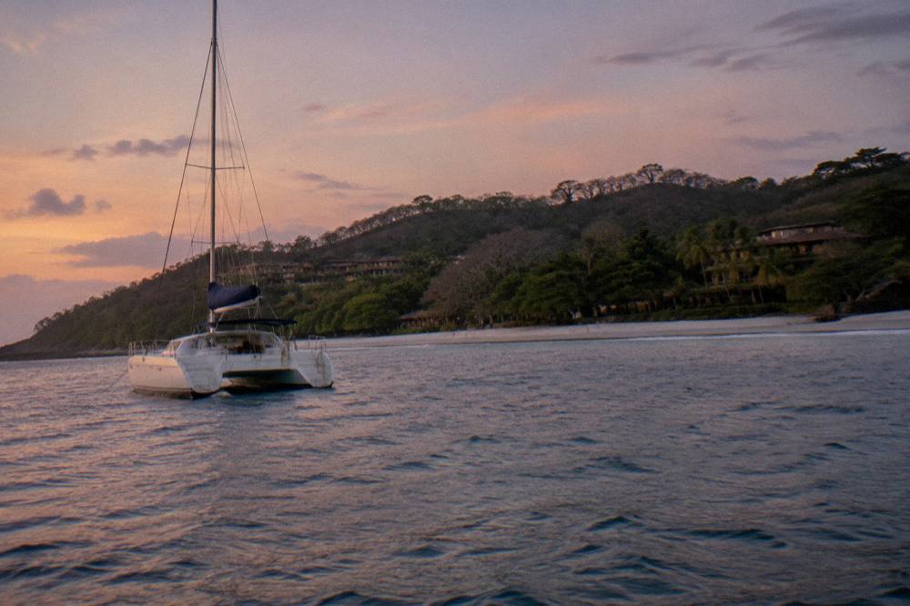 Sunset over calm Pacific water with a catamaran silhouette near shore