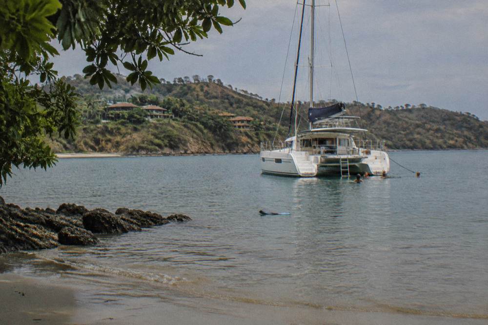 A catamaran moored in a calm bay with guests swimming near the stern
