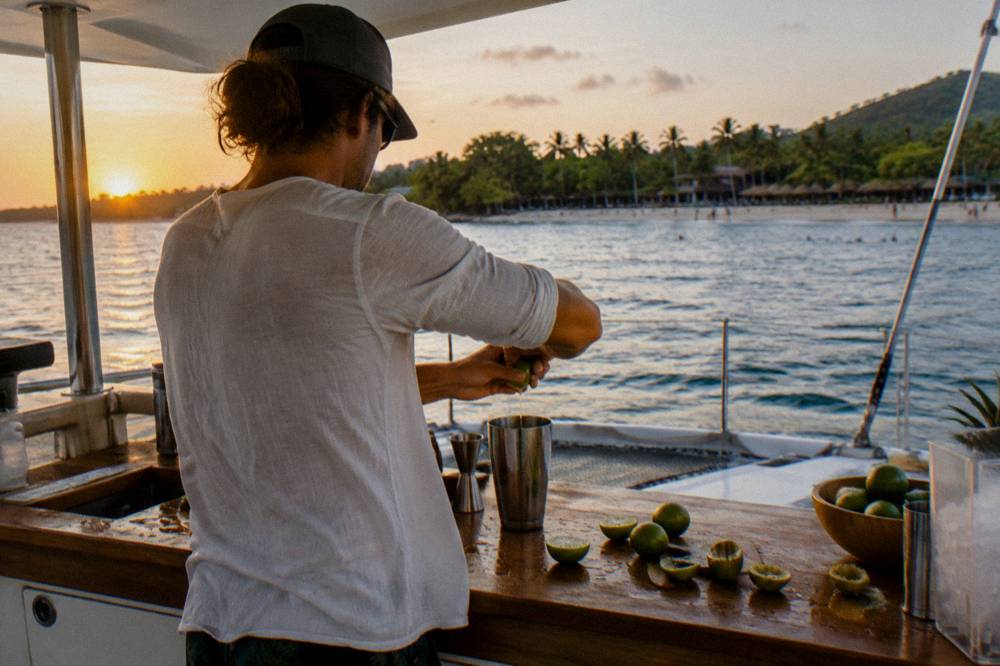 A crew member preparing drinks at an outdoor bar on a catamaran stern