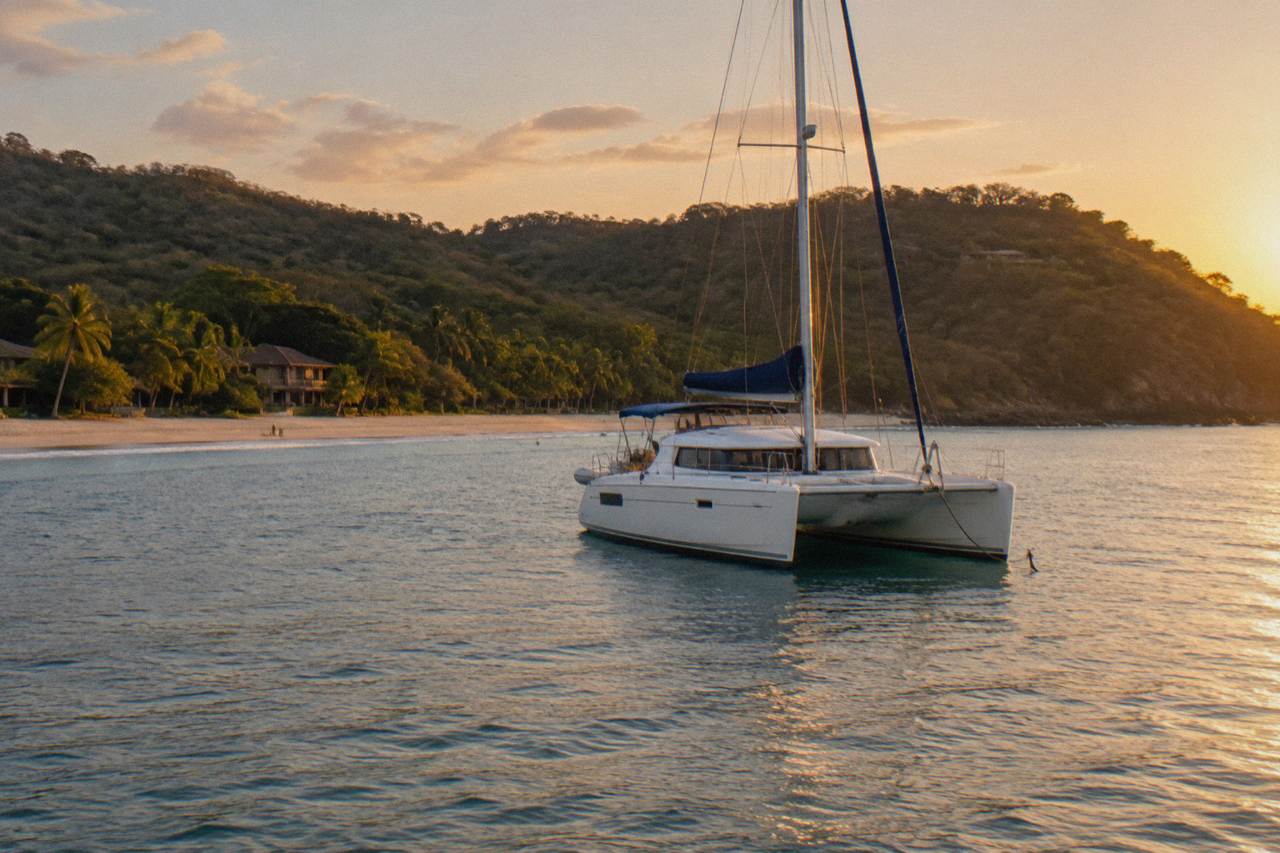 A catamaran anchored near a quiet cove on the Guanacaste coast with forested hills behind