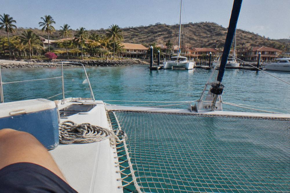 Open-air catamaran deck with netting and railings overlooking calm blue water