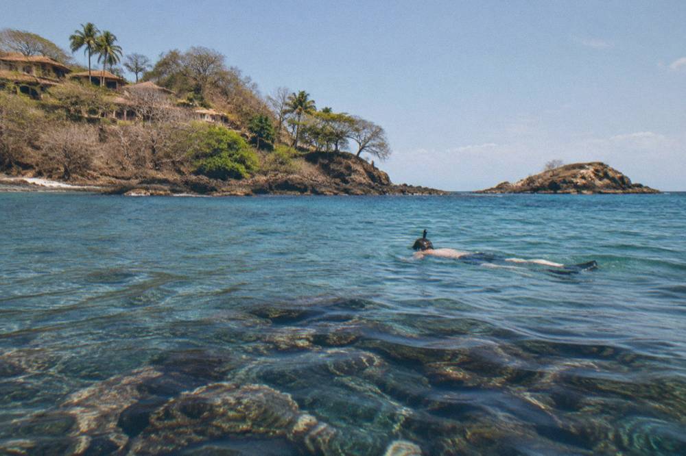 Snorkeler floating over a rocky reef in clear sunlit water