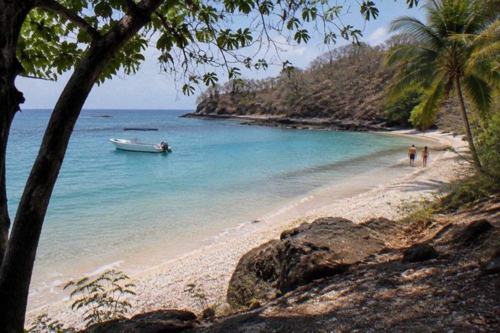 Palm-fringed white sand cove with turquoise water and an anchored boat