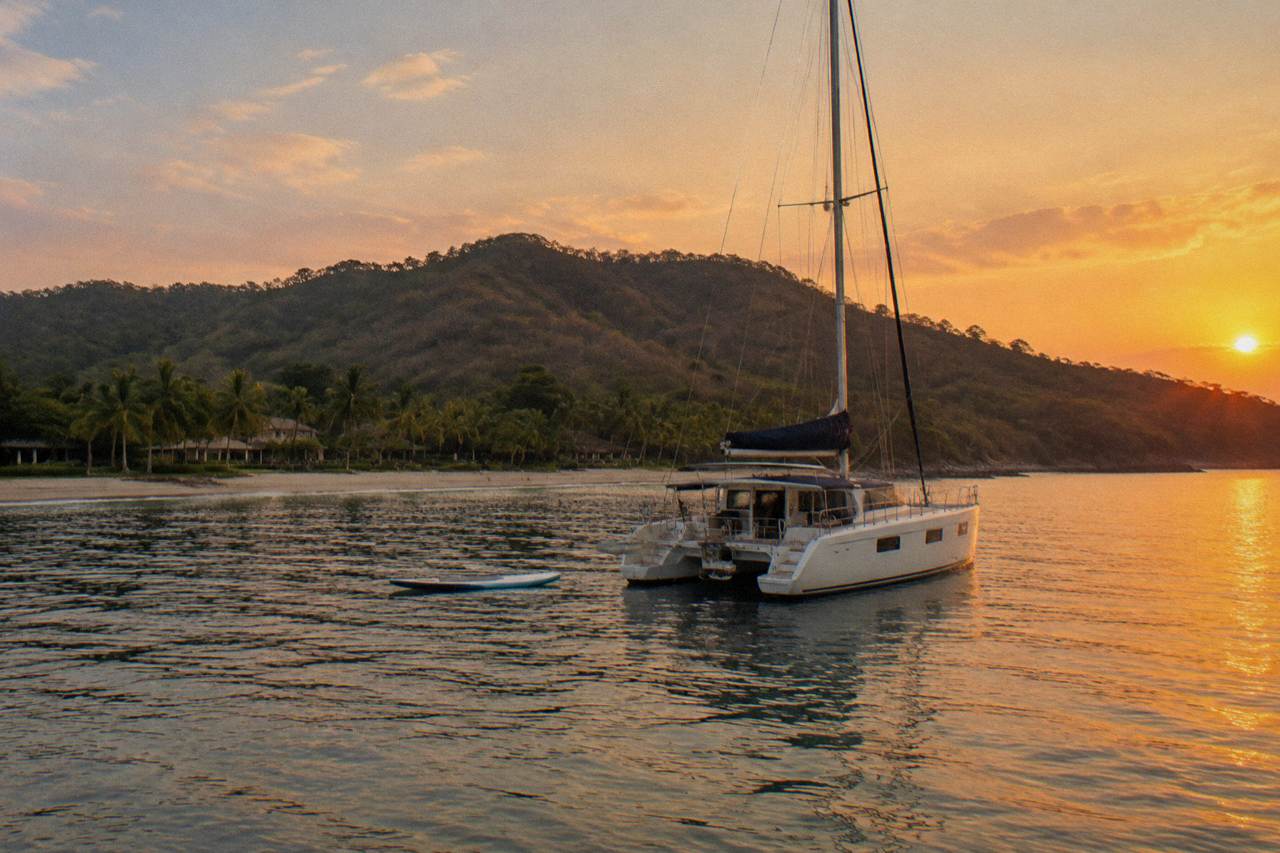 Catamaran anchored in a calm Pacific cove near forested hills at golden hour