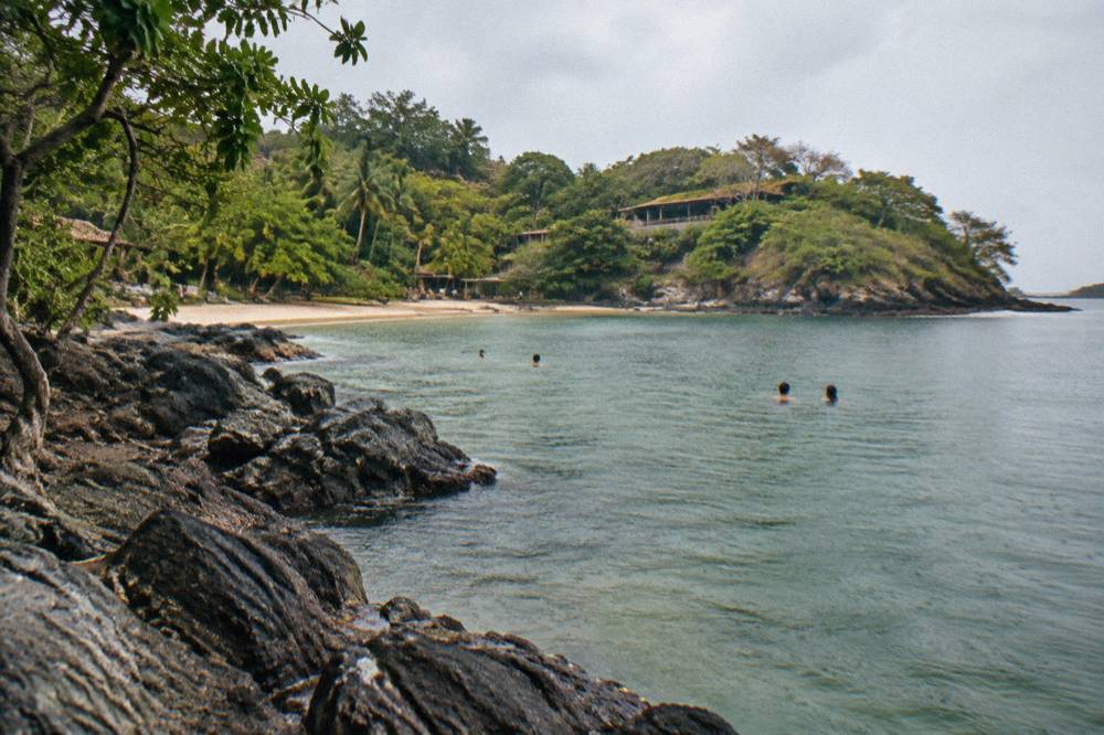 Snorkelers in calm green water beside a rocky point on the Guanacaste coast