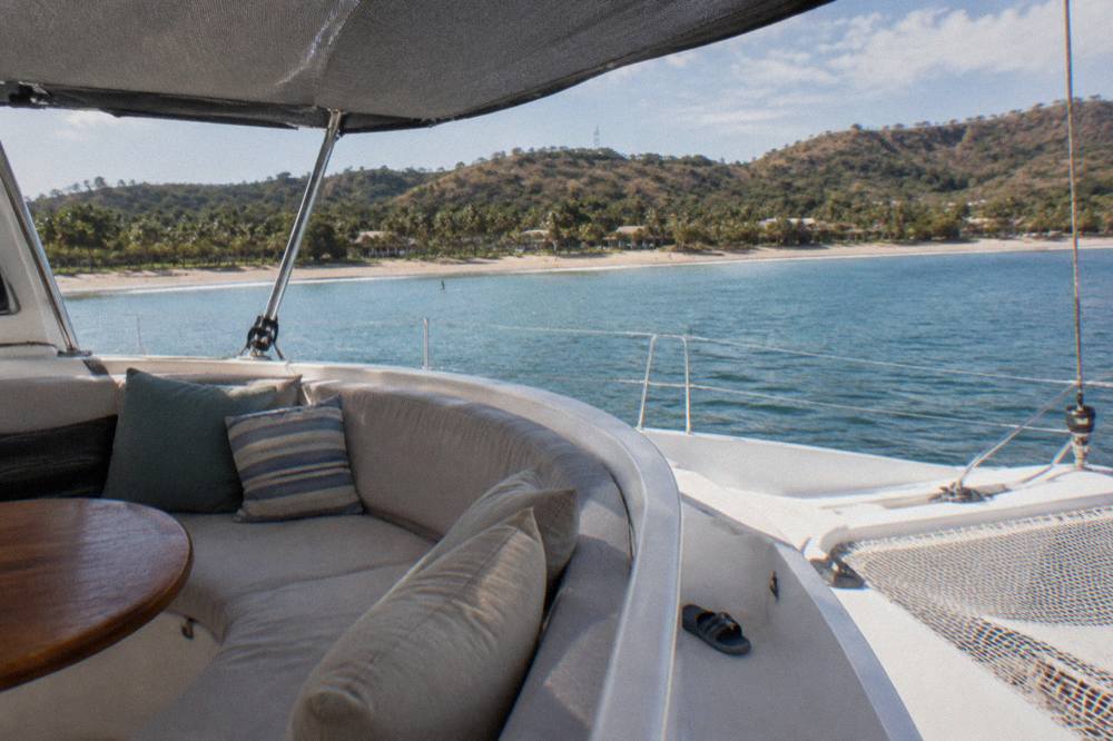 Open deck of a catamaran with lounge seating and netting over calm blue water