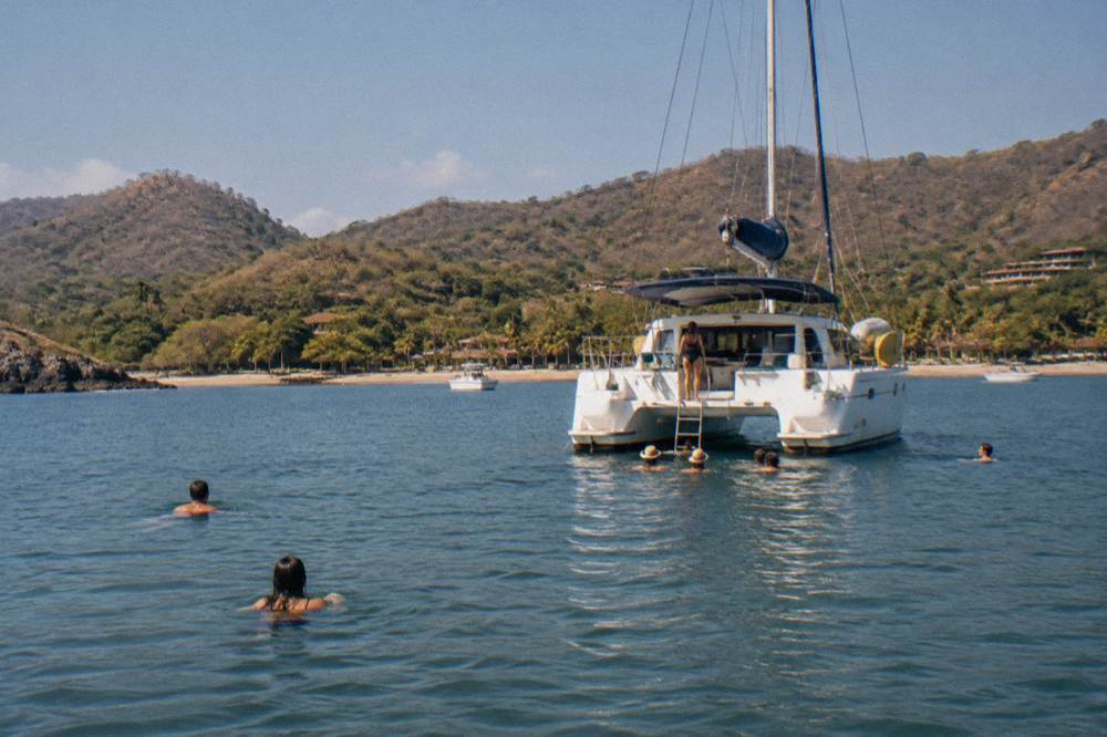 Anchored catamaran in a calm bay with swimmers in the water nearby