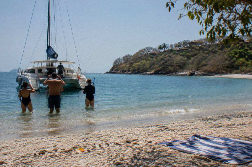 Catamaran moored in a quiet cove with guests preparing to swim