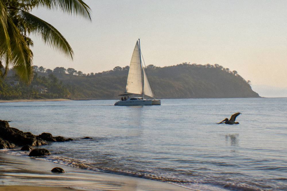 Catamaran under sail on flat morning water with distant islands