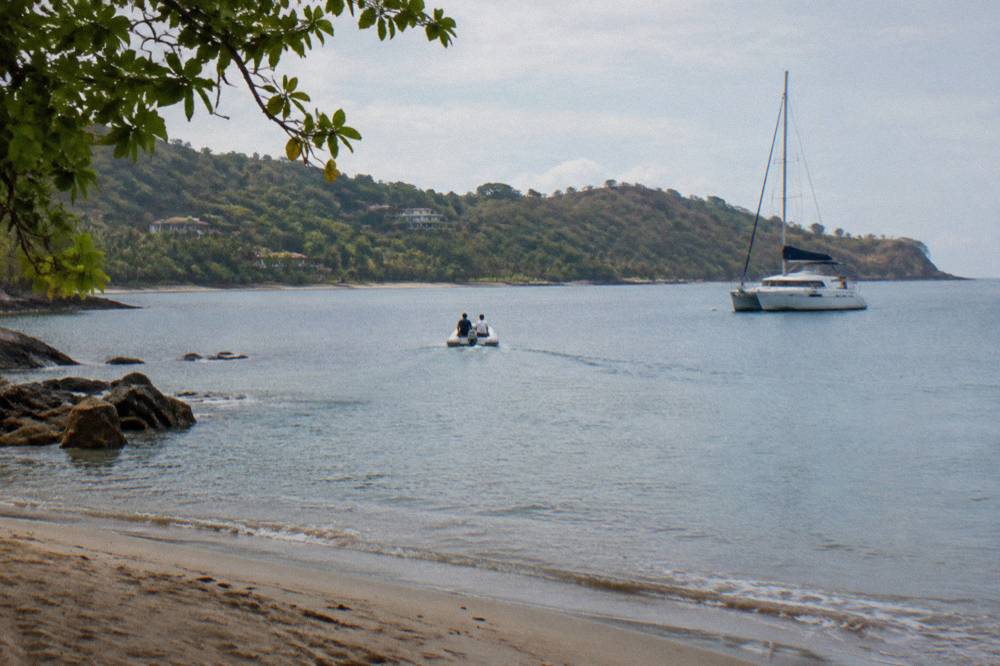 A dinghy carrying passengers from a tropical beach out to an anchored catamaran