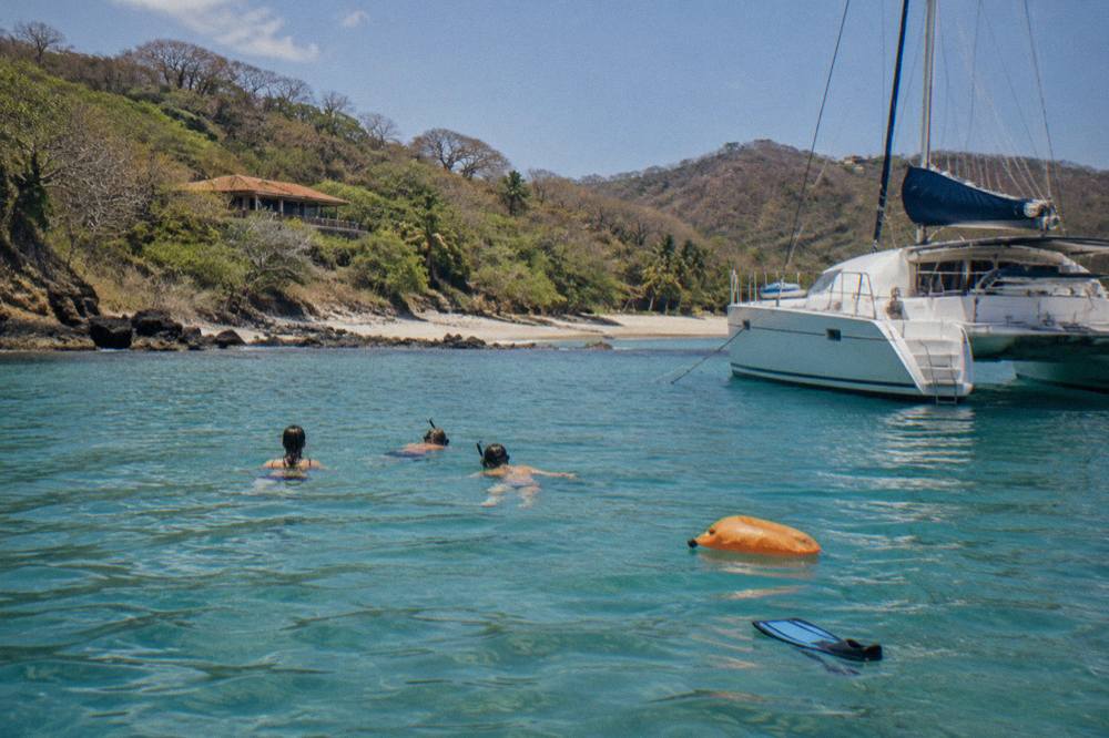 Anchored catamaran with passengers swimming in a calm turquoise cove along the Guanacaste coast