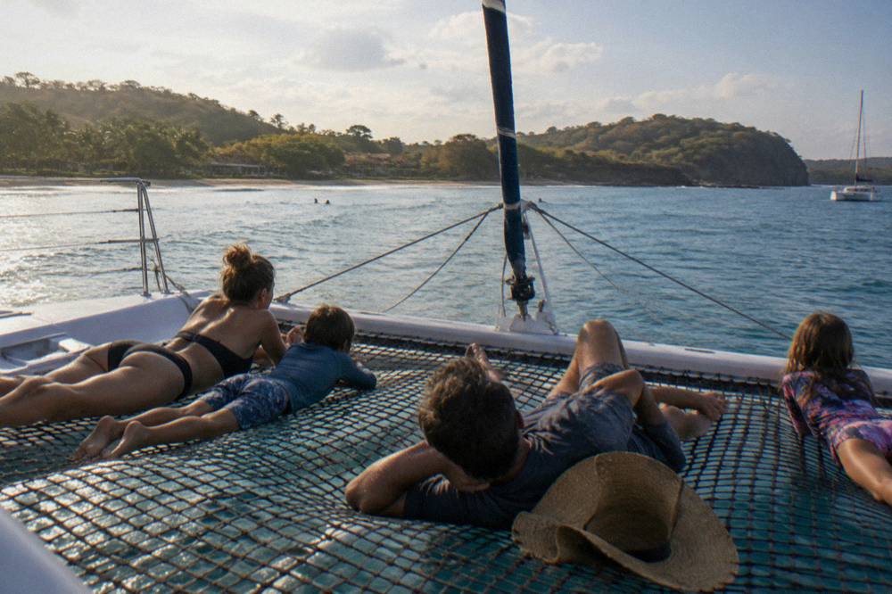 Family relaxing on the trampoline nets of a catamaran in a quiet Guanacaste bay