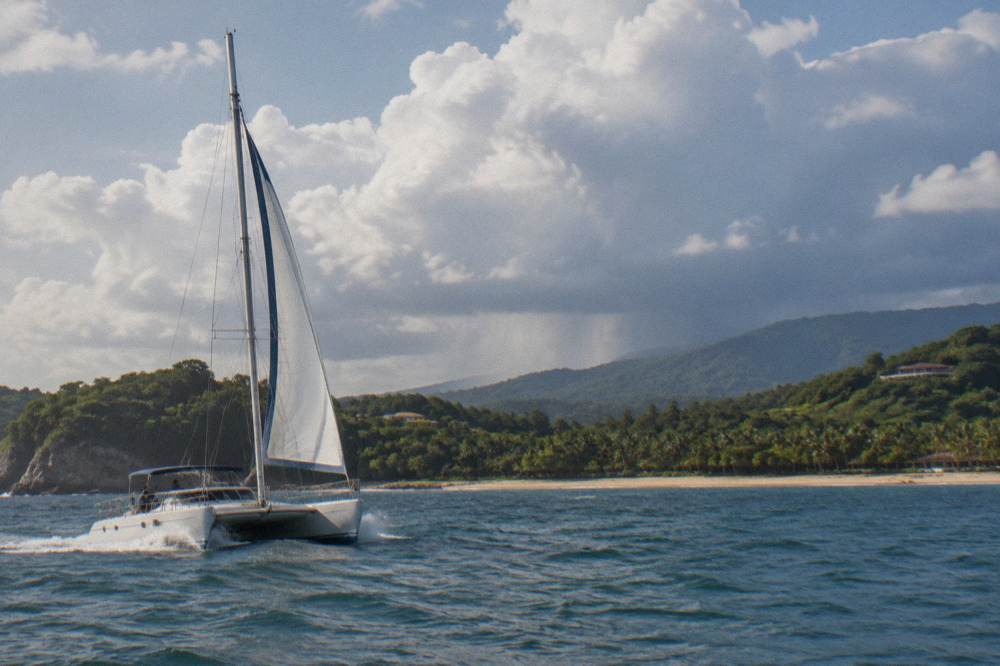 Sailing catamaran underway along the green Guanacaste coastline under building afternoon clouds