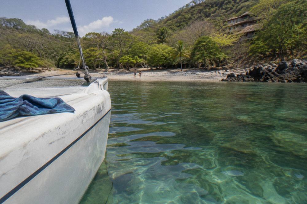 Catamaran anchored in a quiet cove with clear water over rocks