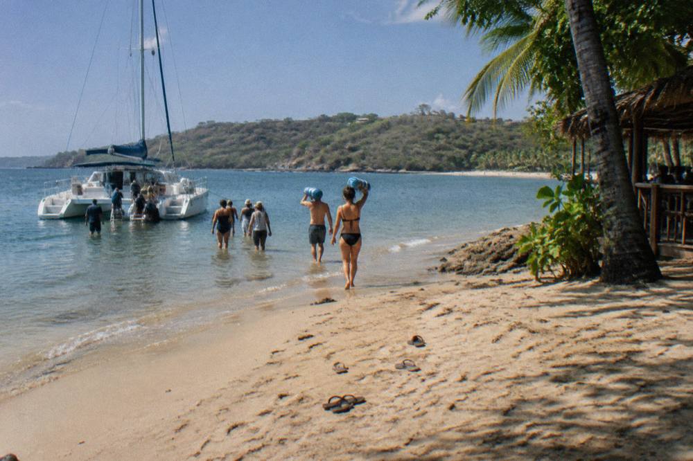 Passengers boarding a catamaran from a quiet beach in the early afternoon