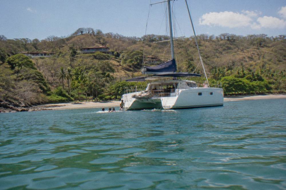 A catamaran at anchor in a quiet bay with passengers in the water near the boat