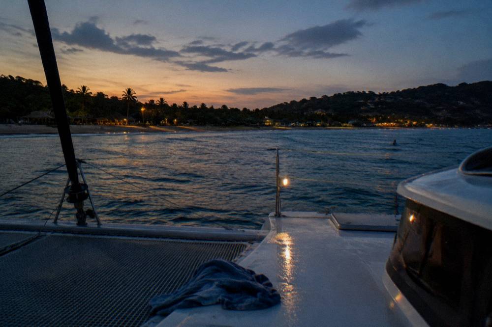 A catamaran deck in the last light of day with the coast in the background