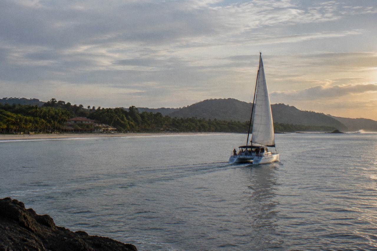 A catamaran under sail on calm Pacific water off the Guanacaste coast in late afternoon light